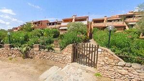A residential area with stone walls, a gate, and terraced houses with red-tiled roofs. - Apartment in Porto Istana Near the Beach (Olbia)