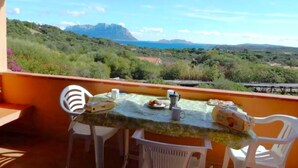 A balcony with a table set for breakfast, overlooking a mountainous landscape and the sea. - Apartment in Porto Istana Near the Beach (Olbia)