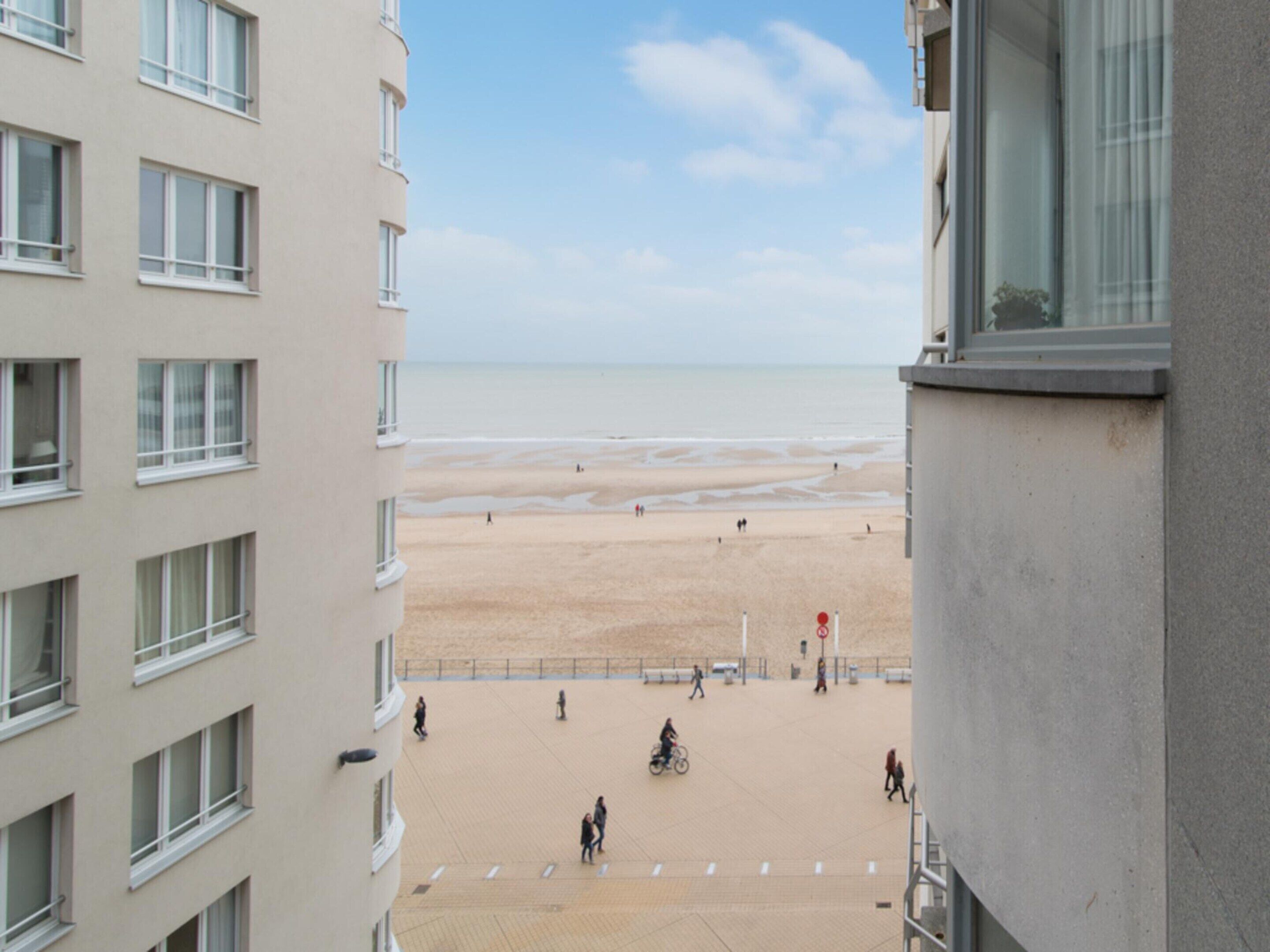 A view from a high-rise building overlooking a sandy beach with people walking and cycling.