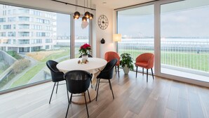 A modern dining area with a round table, black chairs, and a view of a building and a bridge through large windows. - Stylish Apartment With Terrace in Bredene (Bredene)