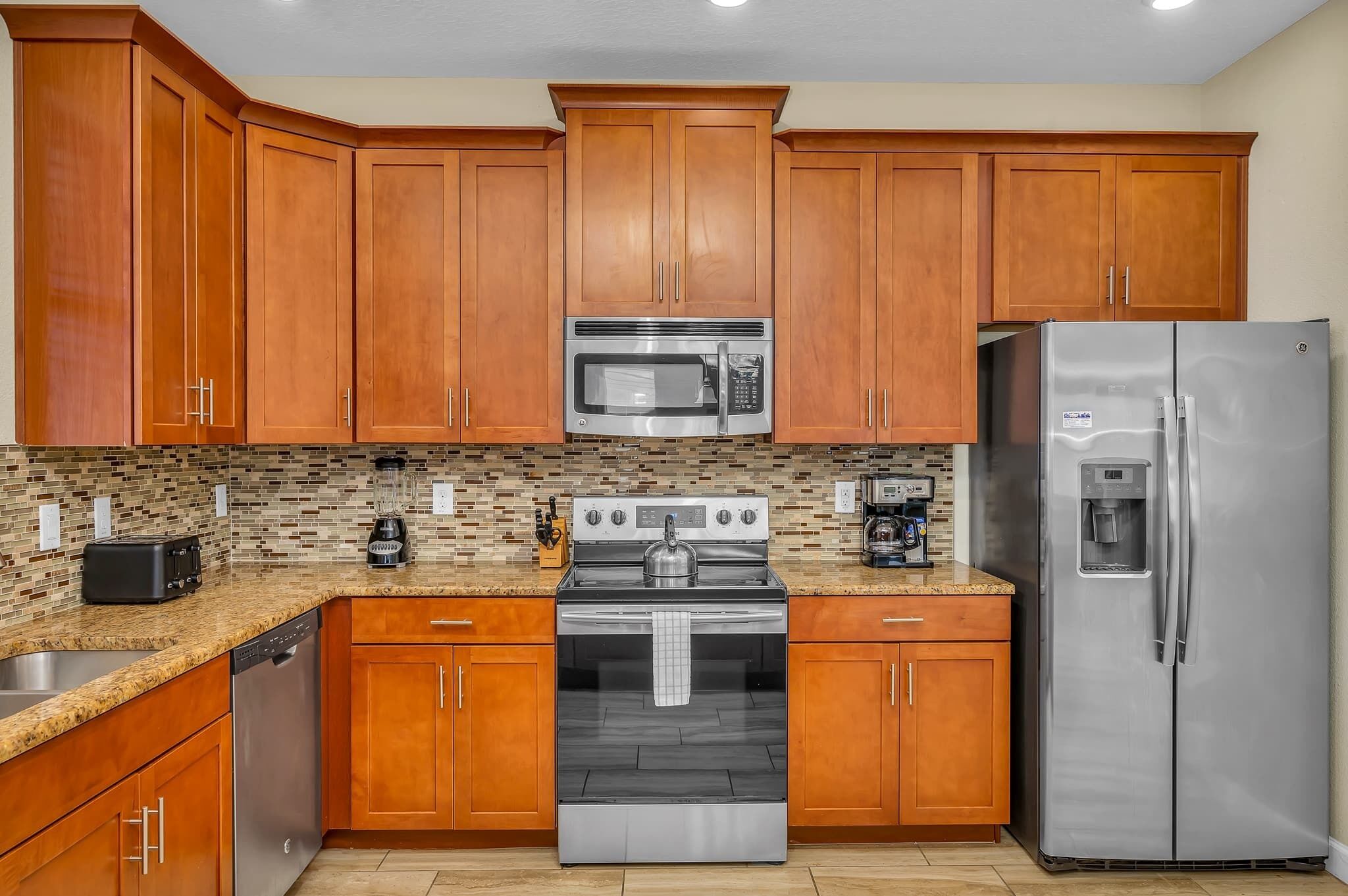 A kitchen with wooden cabinets, a stainless steel refrigerator, a microwave, a stove, and a dishwasher.