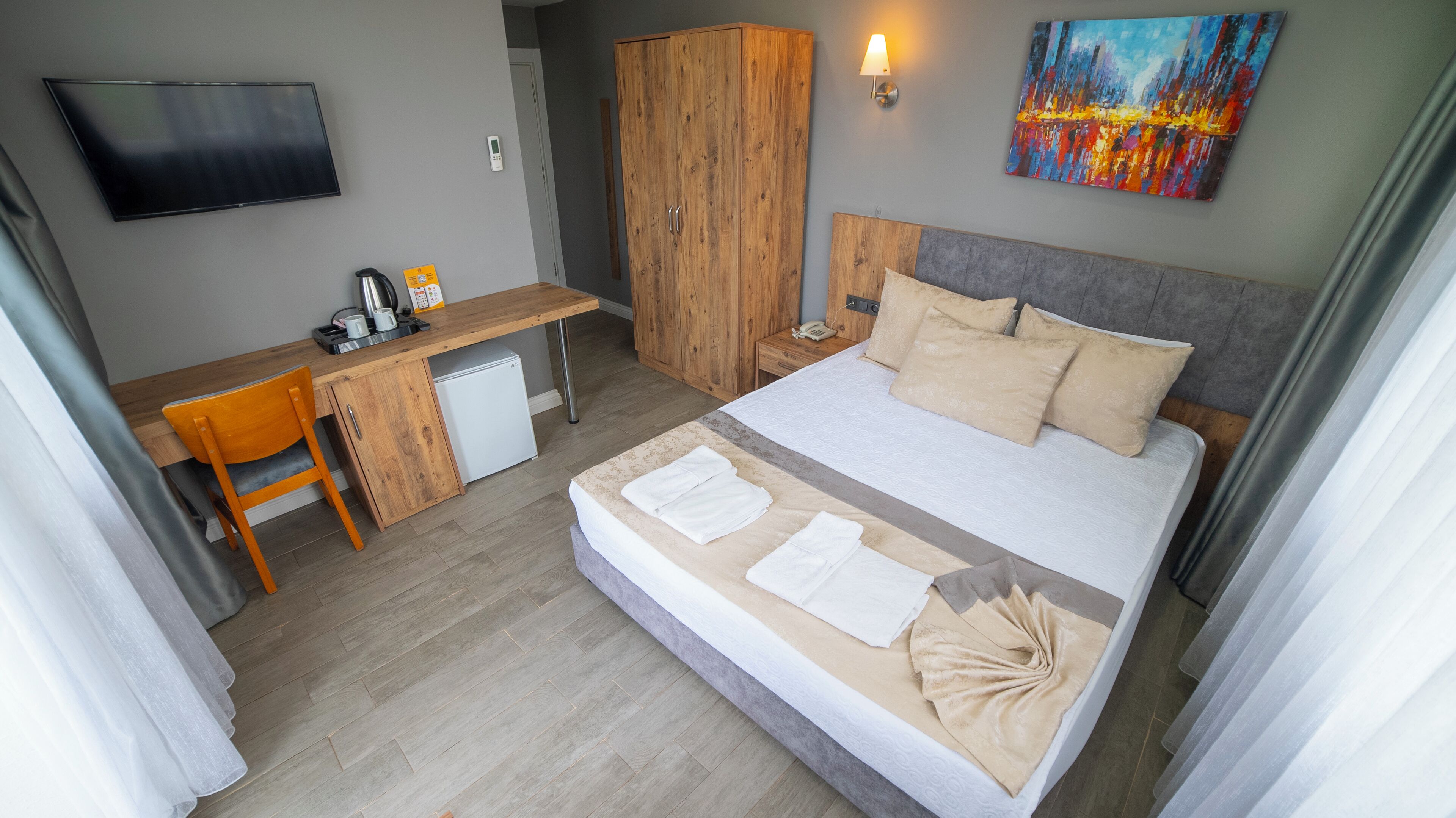 Une chambre d’hôtel avec un lit, un bureau, une armoire, une télévision et un tableau au mur.