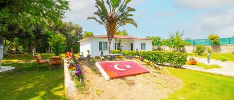 Una casa con jardín, una bandera roja con luna creciente y estrella, y una palmera.