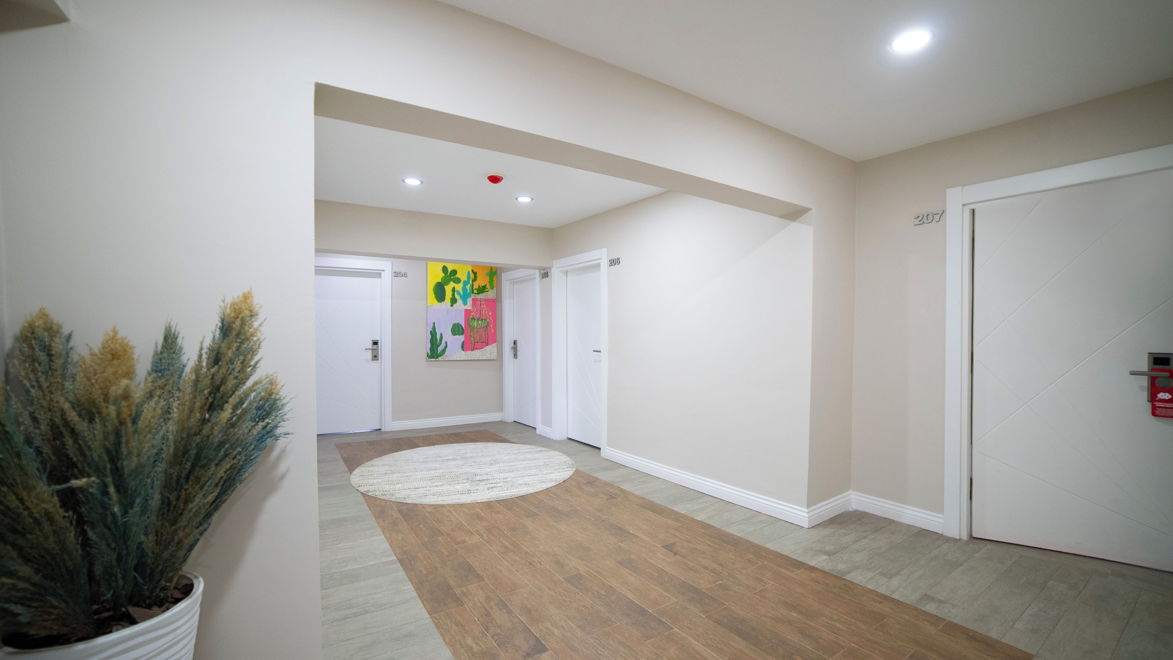 A hallway with wooden flooring, white walls, and a door with the number 208.