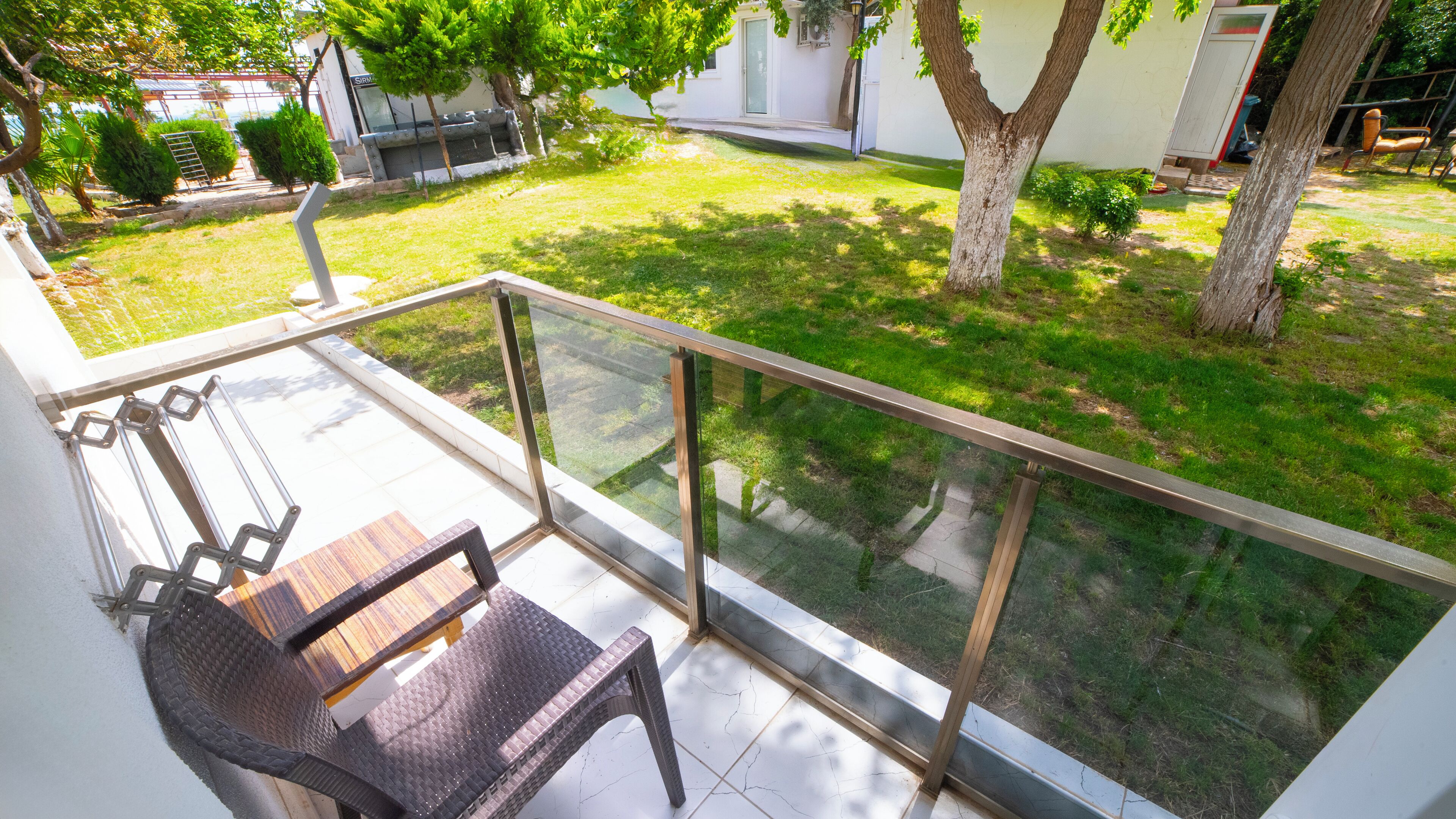 A balcony with a glass railing overlooking a well-maintained lawn and a house in the background.
