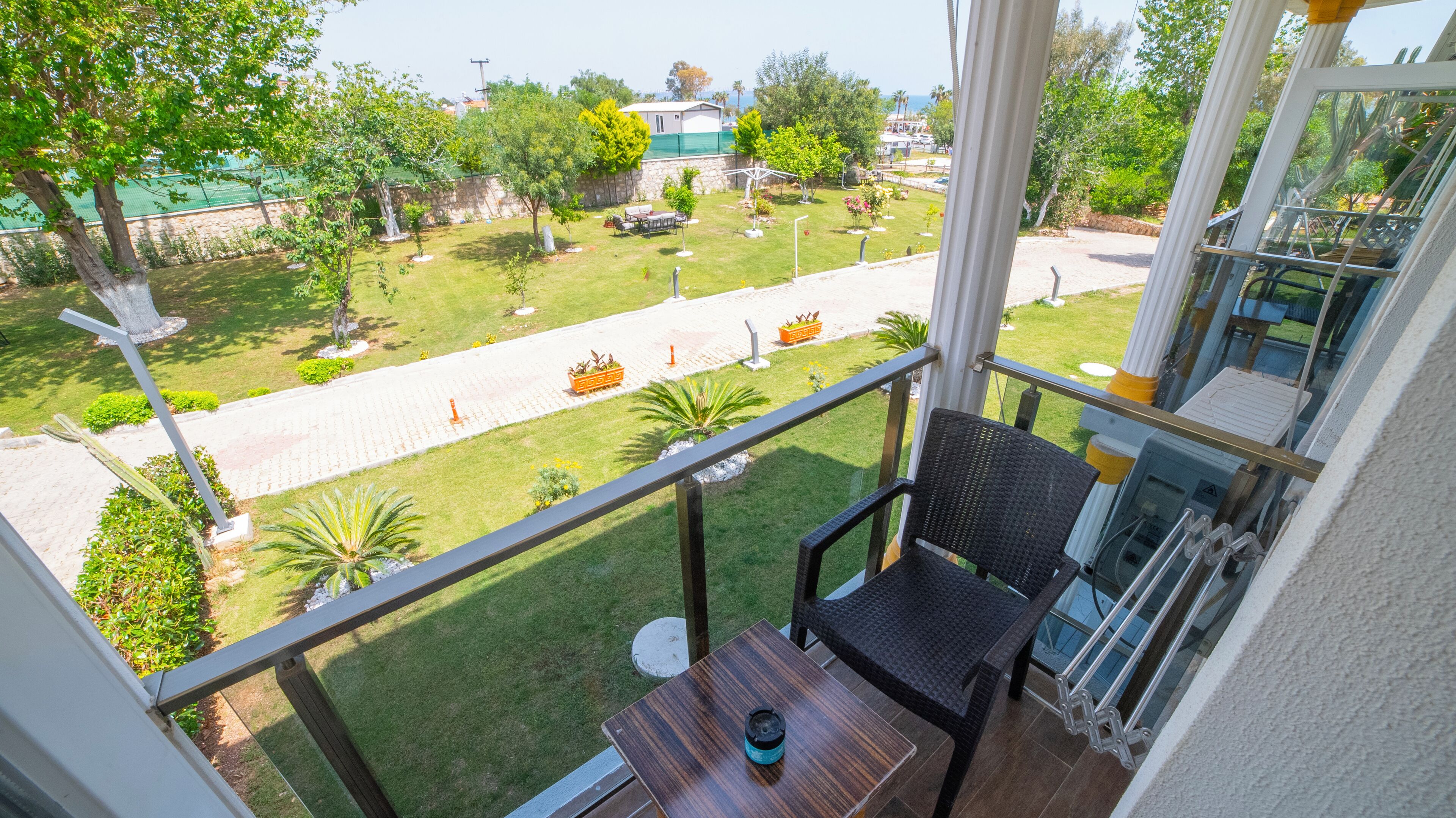 Ein Balkon mit Blick auf einen gepflegten Garten, einen gepflasterten Weg und eine entfernte Straße.