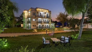 Un hotel de varios pisos llamado "LA CACTUS", con una entrada bien iluminada, una zona de estar al aire libre y un jardín ajardinado.