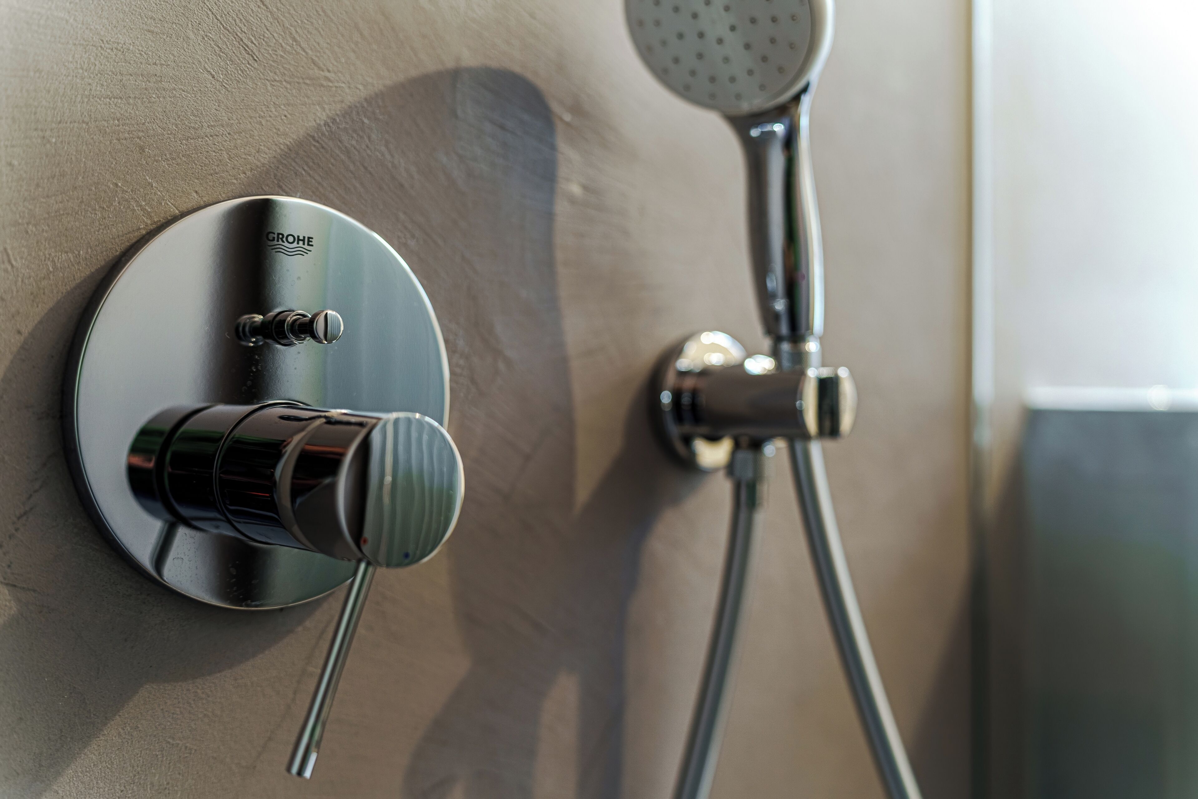 A wall-mounted shower control with a GROHE brand knob and a handheld showerhead.