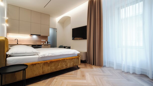 Ein modernes Hotelzimmer mit Bett, kleinem Tisch, Fernseher und Küchenzeile.