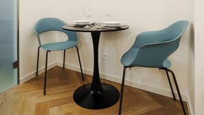 Ein Eckzimmer mit einem runden Tisch, zwei Stühlen, einer Tür und Holzdielen.