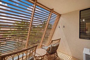 Un balcon doté d’une cloison en lattes de bois, de chaises en osier et offrant une vue sur la verdure.