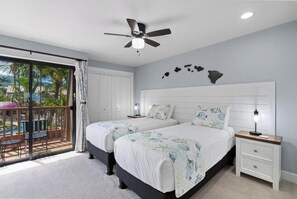 A bedroom with two beds, a ceiling fan, a nightstand, and a view of a balcony with outdoor furniture.