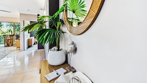 Un interior moderno con un espejo grande, una planta en maceta, una escultura de pájaro y un escritorio de madera con un cuaderno y un bolígrafo.