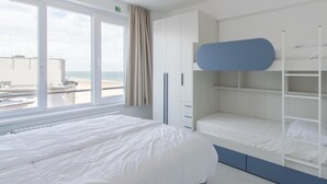 A modern hotel room with a large bed, a bunk bed, and a view of the beach through a large window. - Family Apartment in Ostend Near the sea (Ostend)
