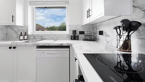 A modern kitchen with white cabinets, a built-in dishwasher, a large window, and a black stove. - Unique 2BR Finchley Flat Sleeps 5 (London)