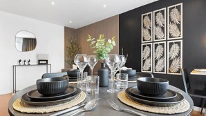 A modern dining area with a round table set for four, featuring black bowls, clear glasses, and silverware. - Unique 2BR Finchley Flat Sleeps 5 (London)