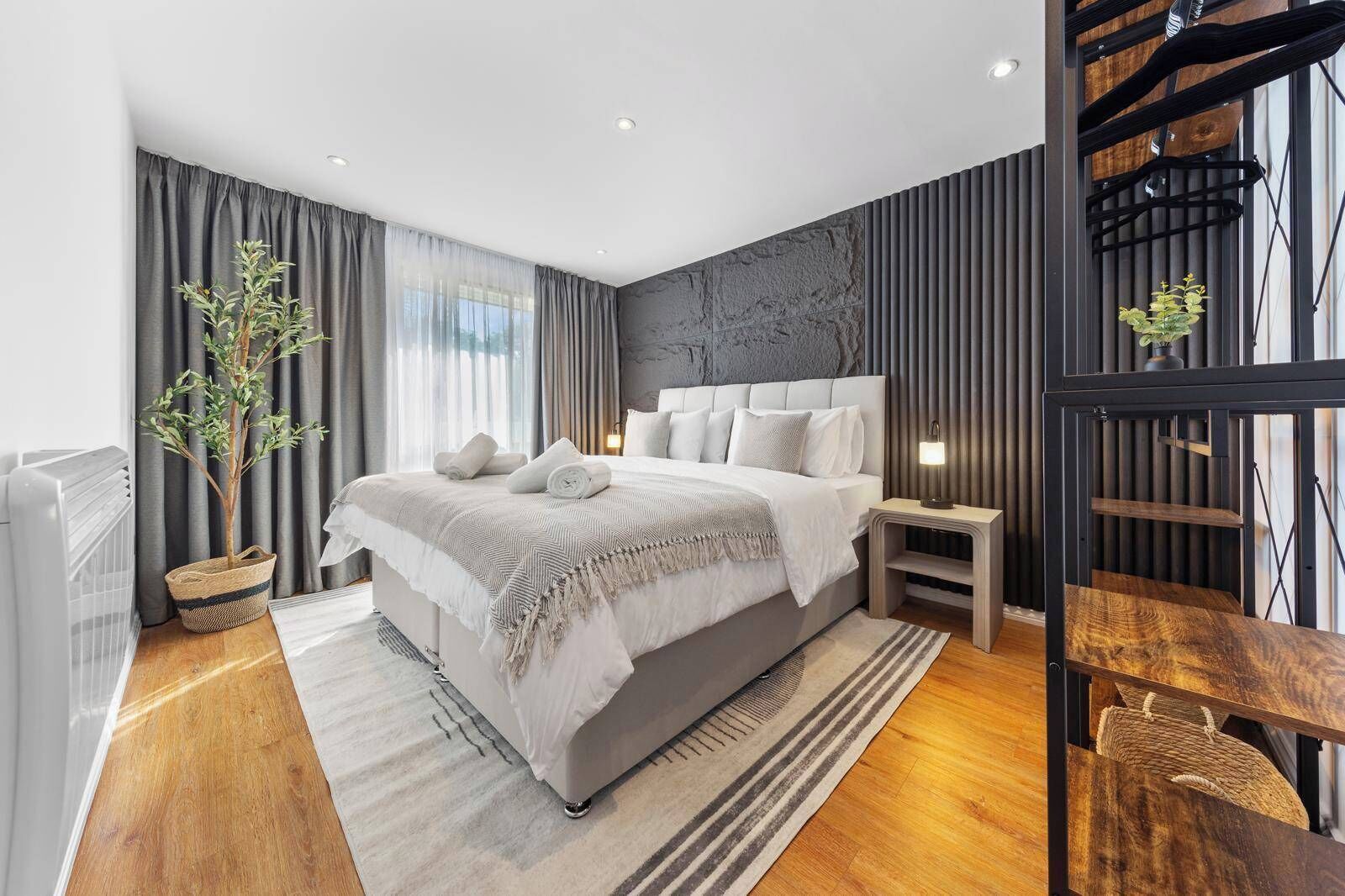 Une chambre moderne avec un grand lit, une table de chevet, un radiateur, une plante en pot et une étagère fixée au mur.