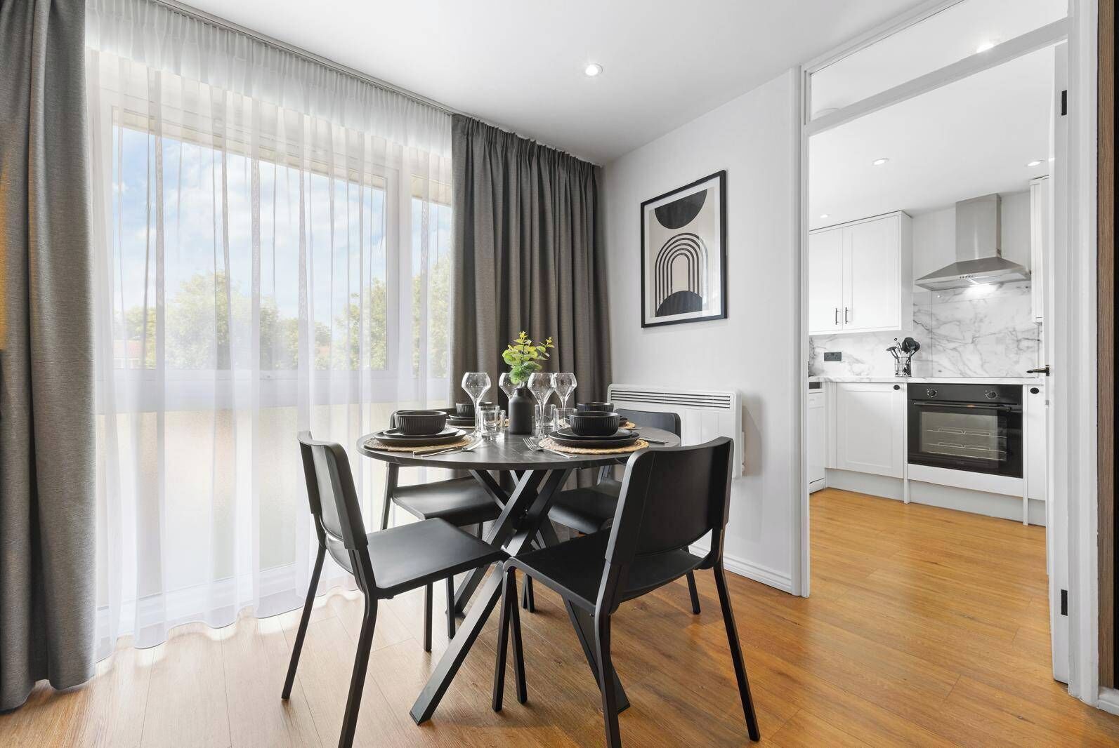 A modern dining area with a round table, black chairs, and a view of the kitchen.
