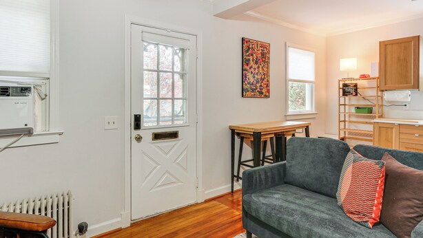 A cozy living room with a grey sofa, a wooden coffee table, and a door with a window. - Walk Downtown: Takoma Park Escape w/ Large Yard! (Takoma Park)