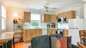 A compact kitchen with wooden cabinets, a microwave, a refrigerator, and a dining area with a table and chairs. - Walk Downtown: Takoma Park Escape w/ Large Yard! (Takoma Park)
