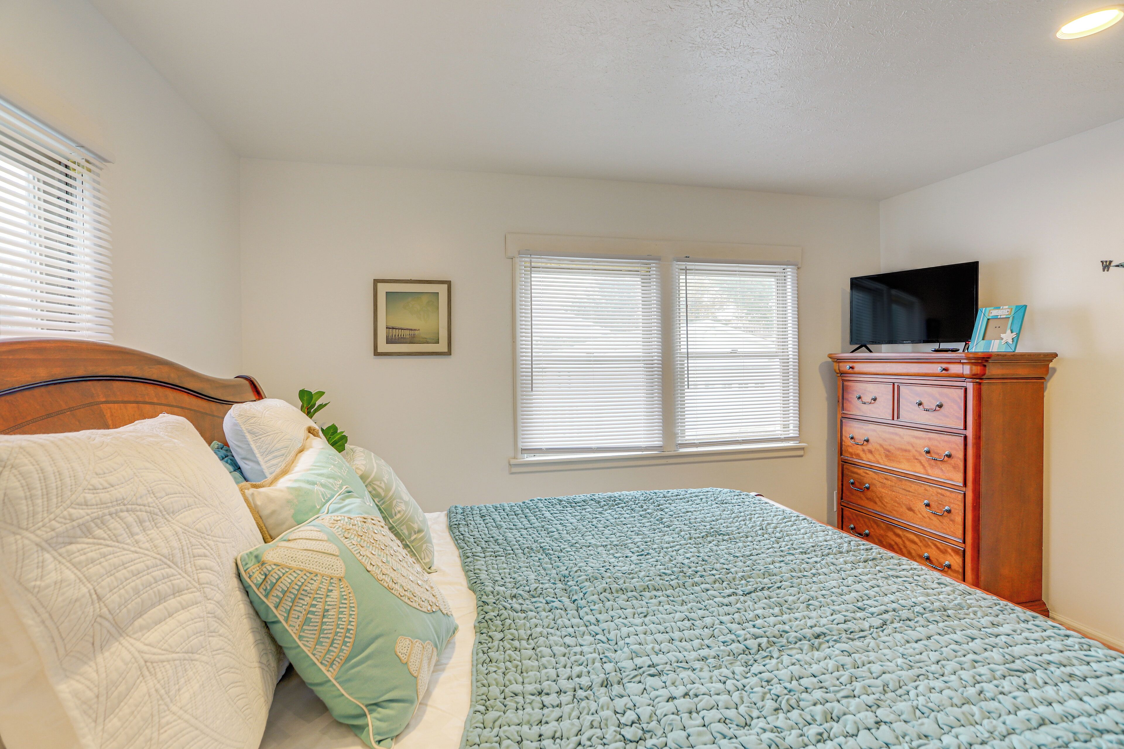 A bedroom with a bed, a dresser, a television, and a window with blinds.