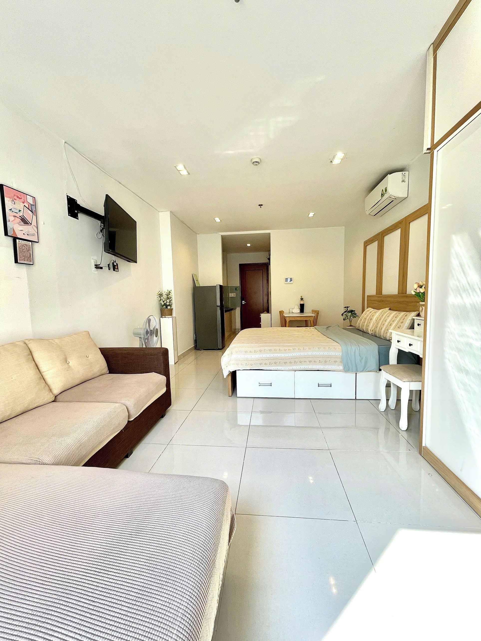A modern bedroom with a bed, a sofa, a TV mounted on the wall, and a small table.