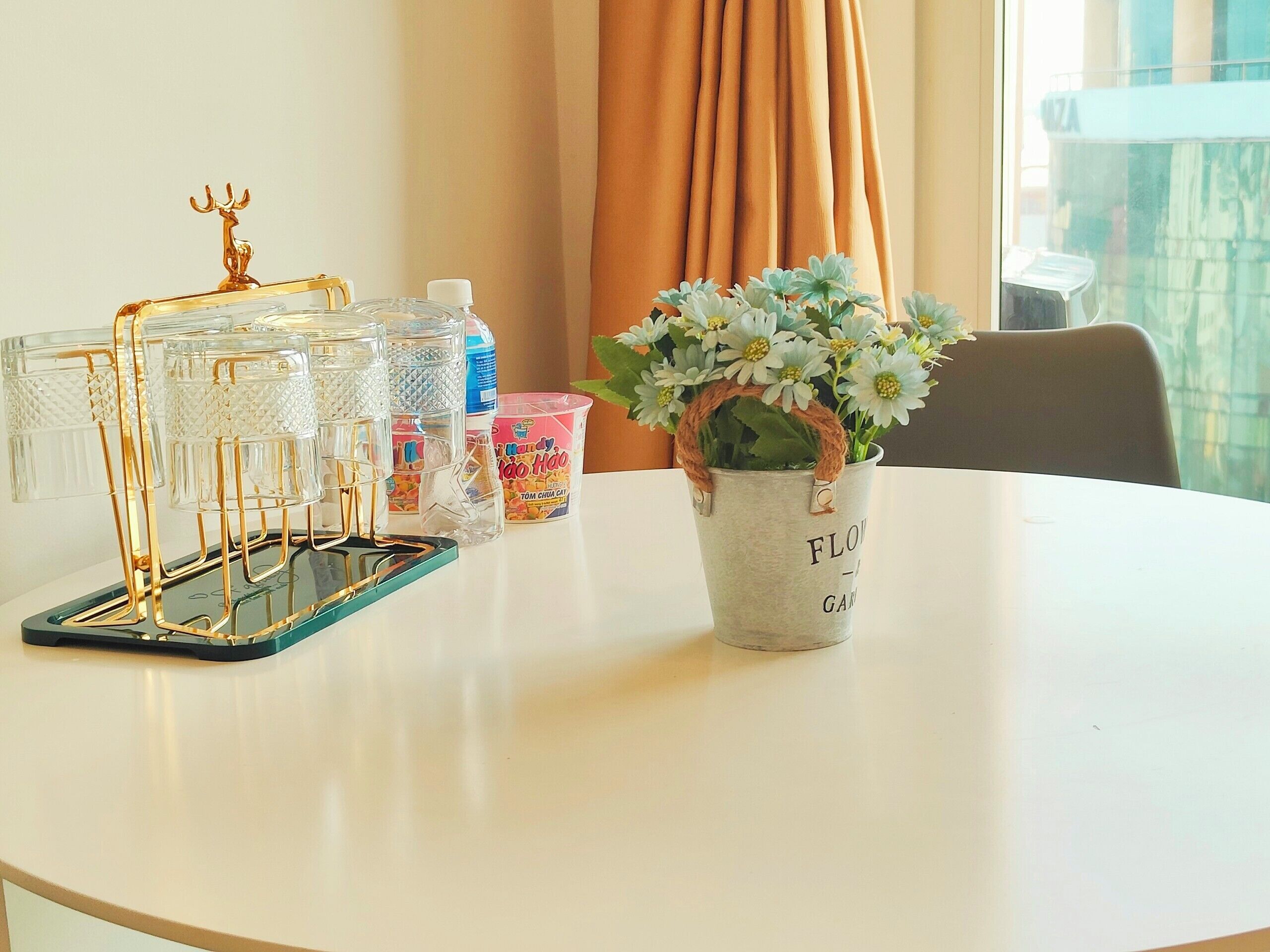 A round table with a glass phone stand, a metal vase with flowers, and a water bottle.