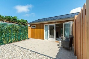 Et moderne hus med terrasse, træhegn og et overdækket udendørs siddeområde.