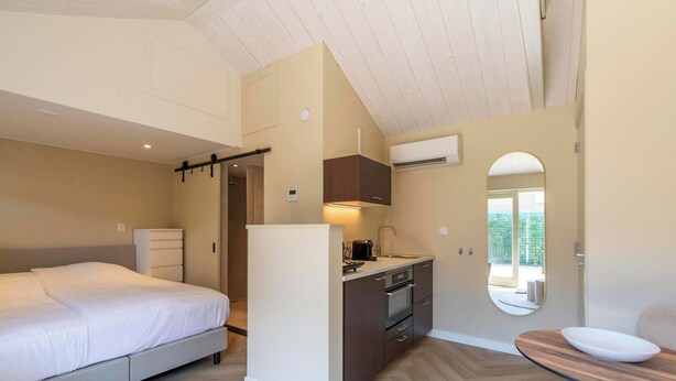 A compact bedroom with a bed, a small kitchenette, and a dining area with a table and chairs. - Beautiful Suite on the Village Square (Callantsoog)