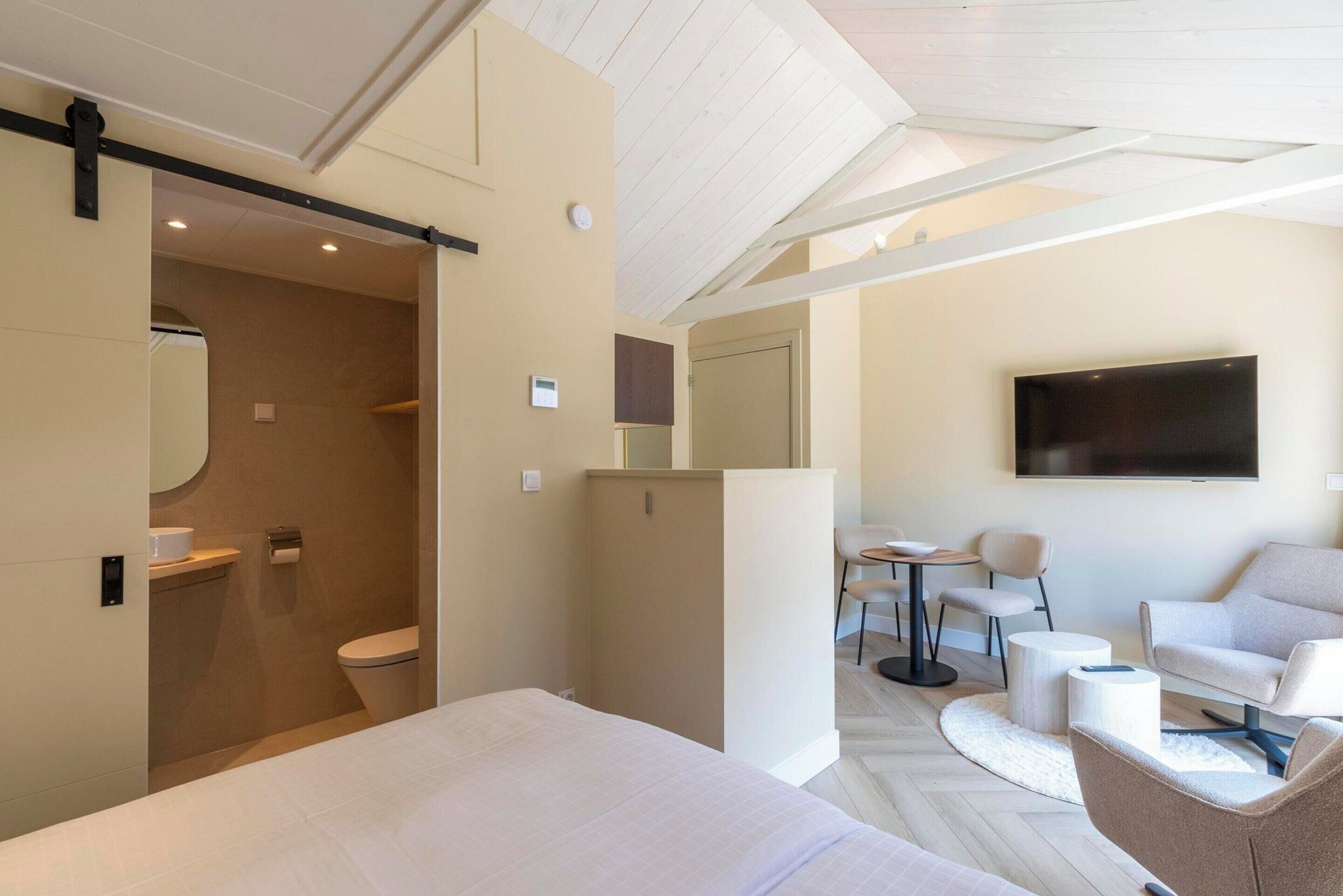 A modern hotel room with a large bed, a seating area with a TV, and a separate bathroom.