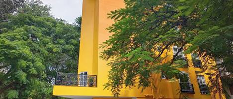 Un edificio amarillo con varias ventanas y balcones, rodeado de árboles y automóviles estacionados.