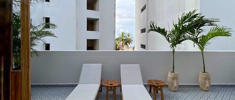A rooftop terrace with two sun loungers, a small round table, and two potted plants.