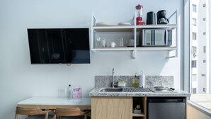 Eine kompakte Küche mit Flachbildfernseher, Mikrowelle und Kaffeemaschine auf einer Ablagefläche.