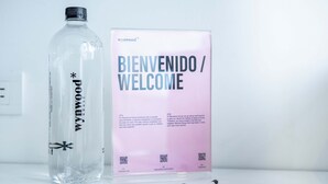 Eine klare Plastikflasche mit dem Aufdruck 'wynwood*' und ein Willkommensschild mit Text und QR-Codes.