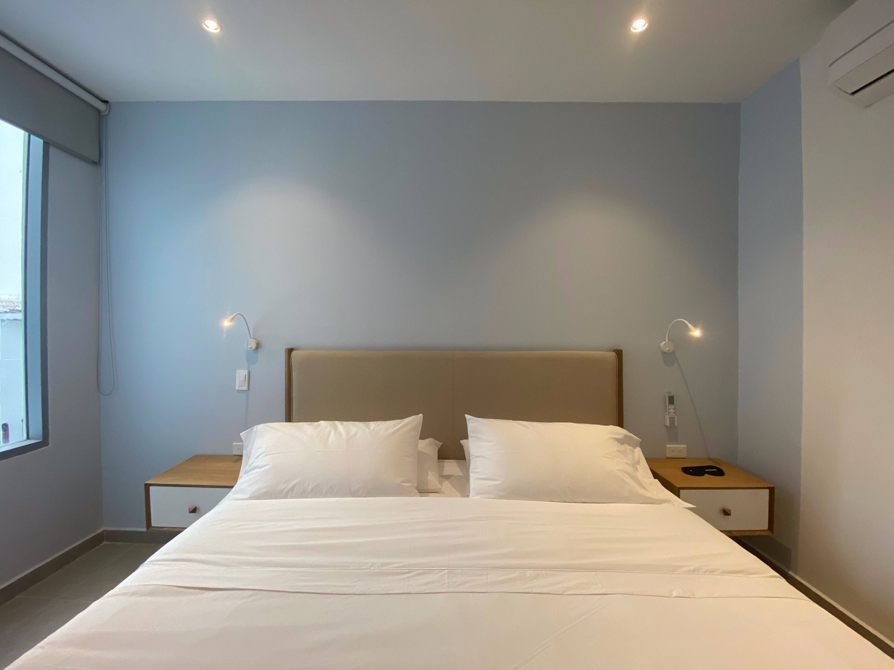 A modern hotel room with a large bed, two bedside tables, and a window providing natural light.
