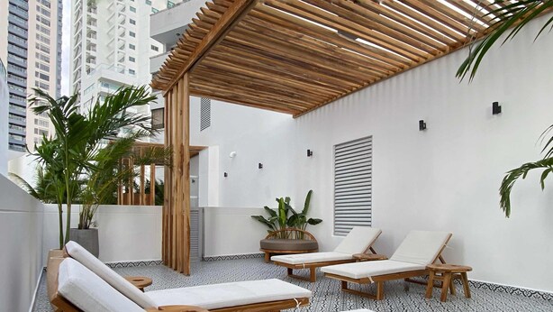 A rooftop lounge area with wooden loungers, potted plants, and a pergola.