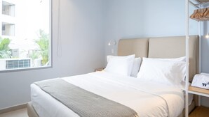 A hotel room with a bed, a bedside table, a wardrobe, and a window with a view of buildings and greenery.