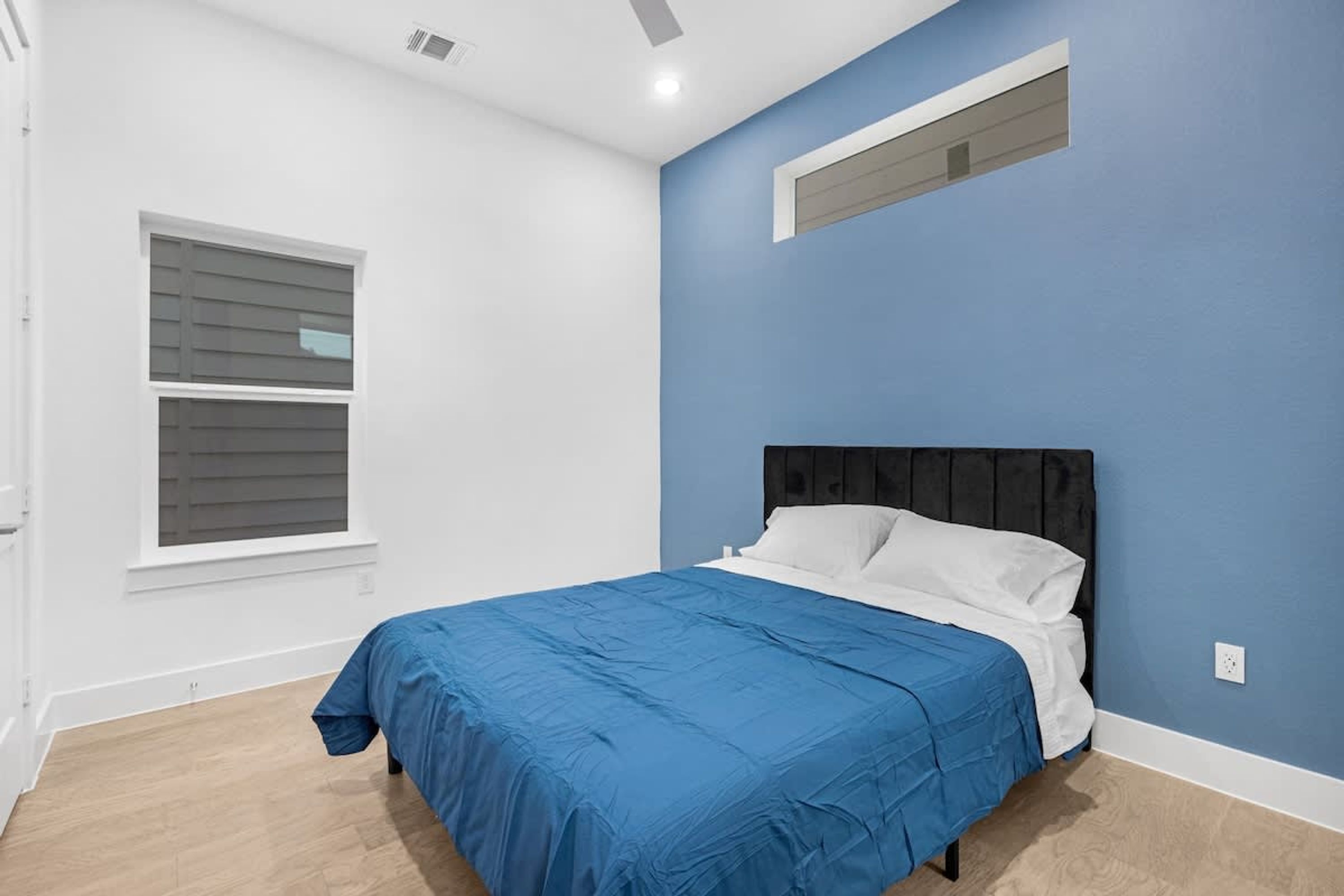 Un dormitorio con cama, ventana y lámpara fijada a la pared.