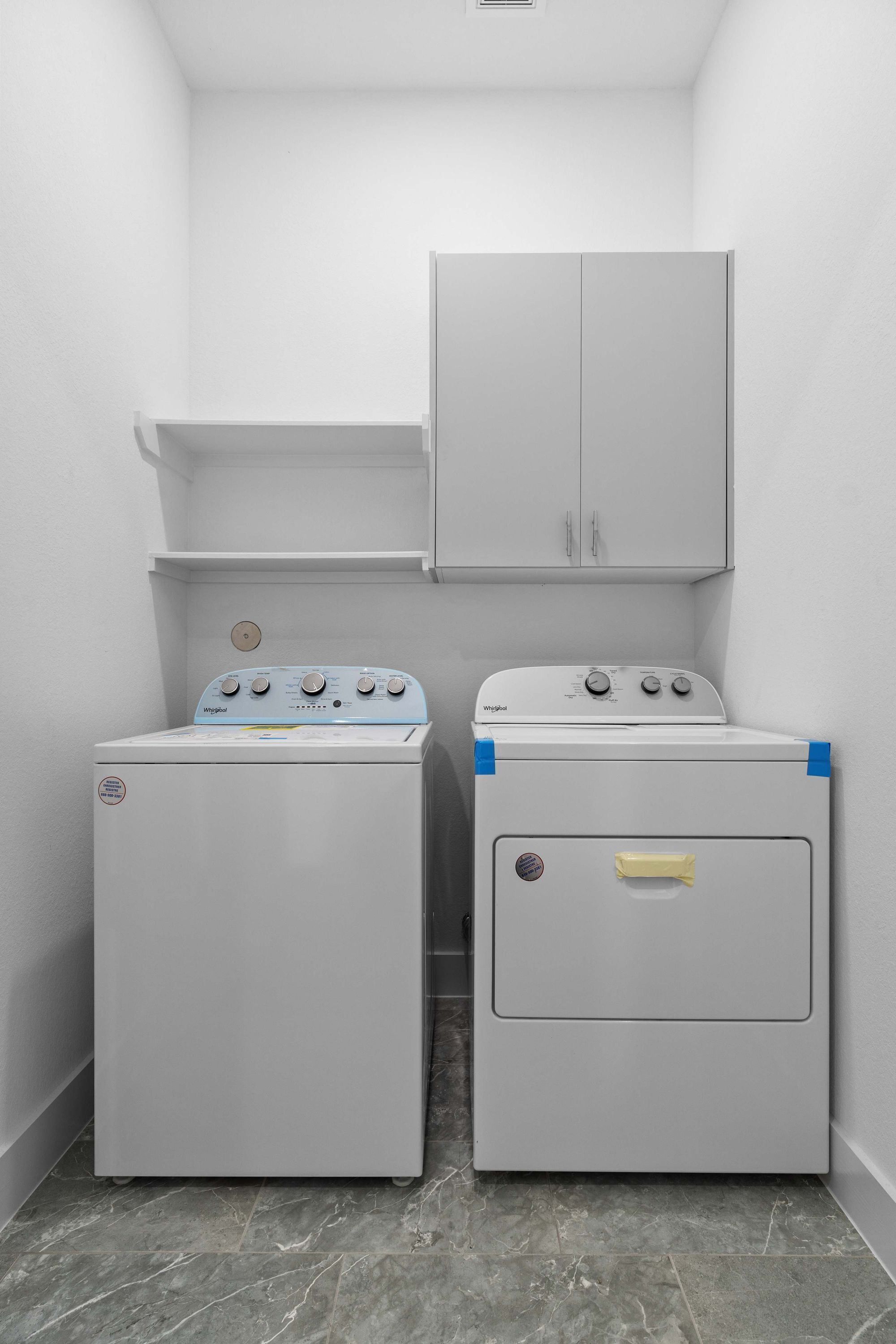 Ein Waschraum mit zwei Waschmaschinen mit Frontlader und einem Schrank darüber.