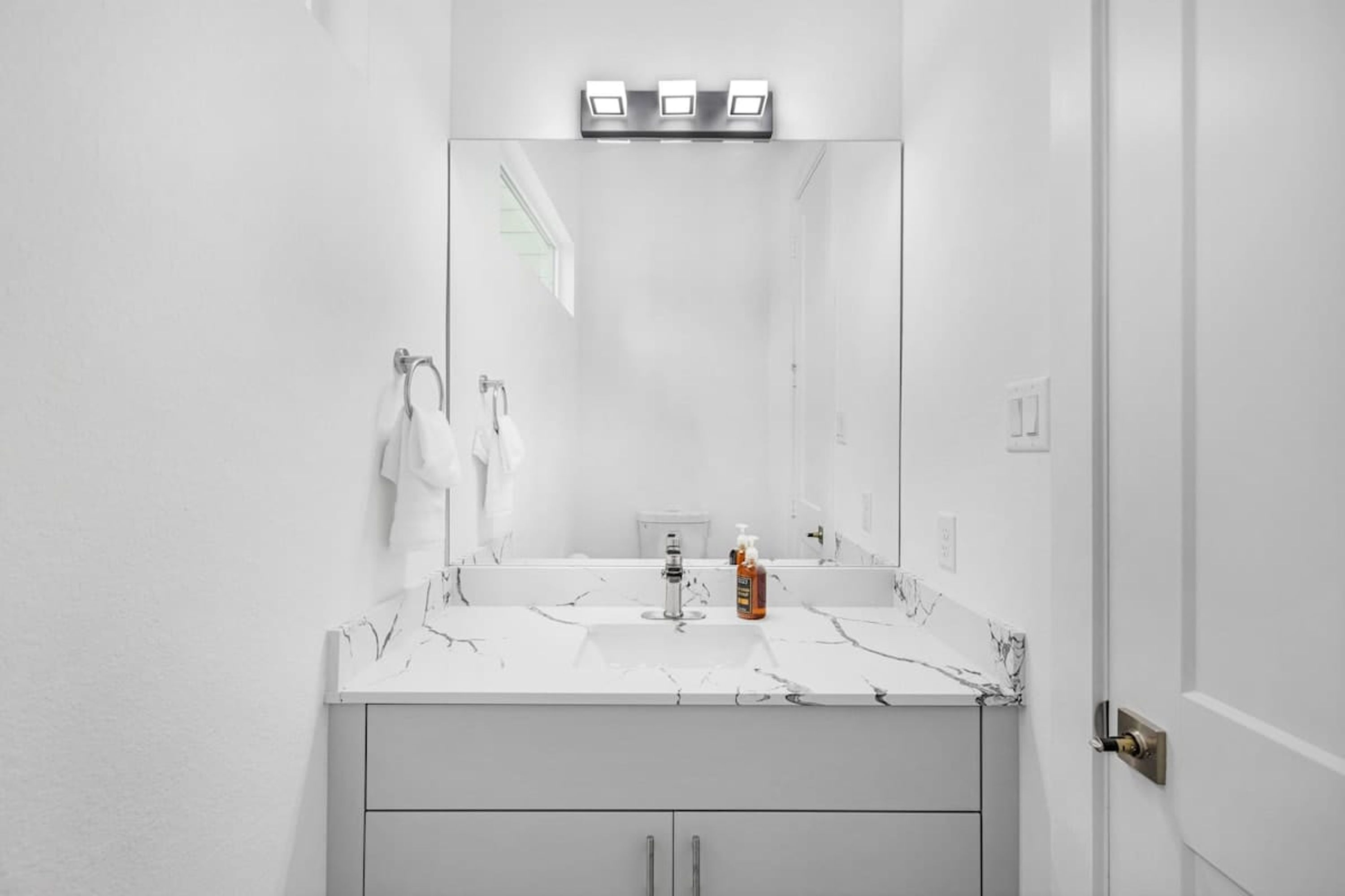 A modern bathroom with a white vanity, a large mirror, and a marble countertop.