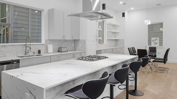 A modern kitchen with a large island, bar stools, and a dining area with a table and chairs. - Luxurious 3 Bed3 Bath Near Downtown Houston (Houston)