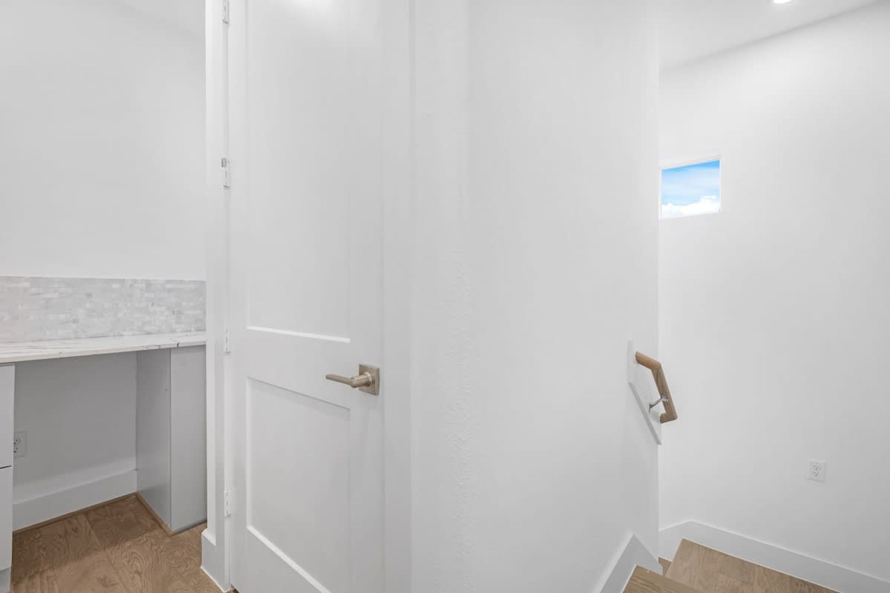 A clean, white-walled room with a wooden floor, a white countertop, and a door with a wooden handle.