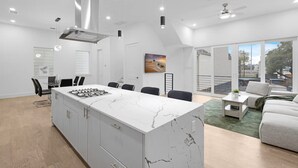A modern kitchen with a marble island, a dining area with chairs, and a living room with a sofa and a view of the outdoors. - Luxurious 3 Bed3 Bath Near Downtown Houston (Houston)