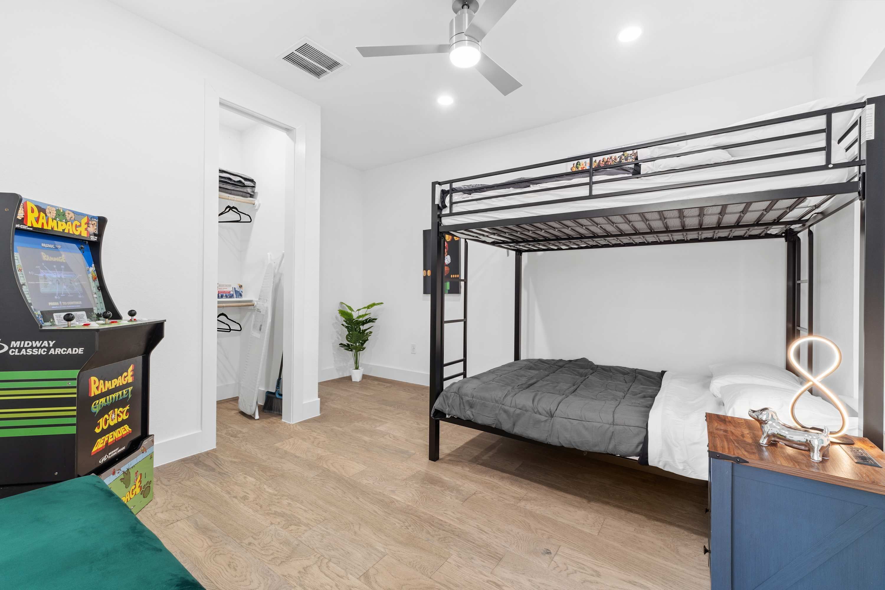 A bunk bed room with a ceiling fan, a small plant, and a classic arcade game.