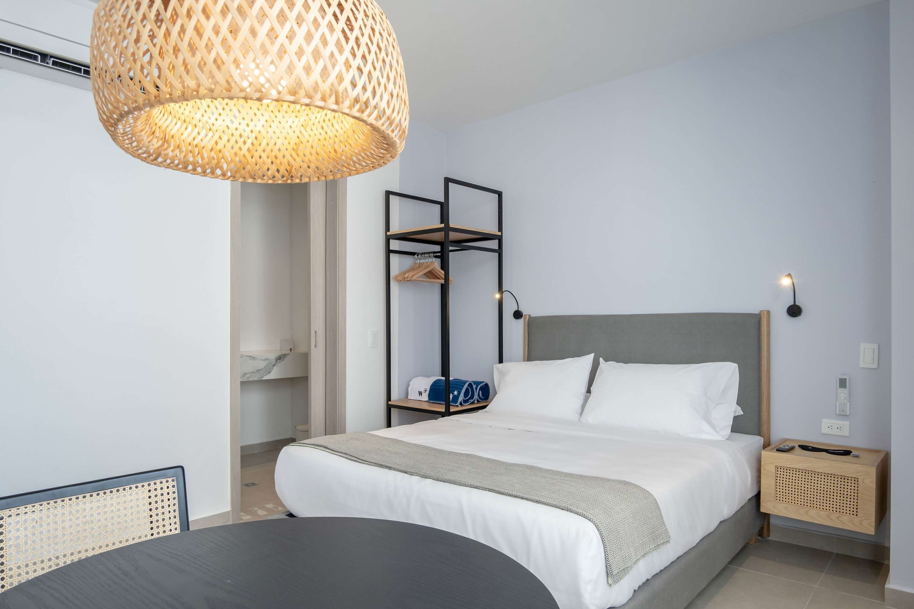 A modern bedroom with a large bed, a hanging rattan light fixture, a wooden nightstand, and a built-in shelving unit.