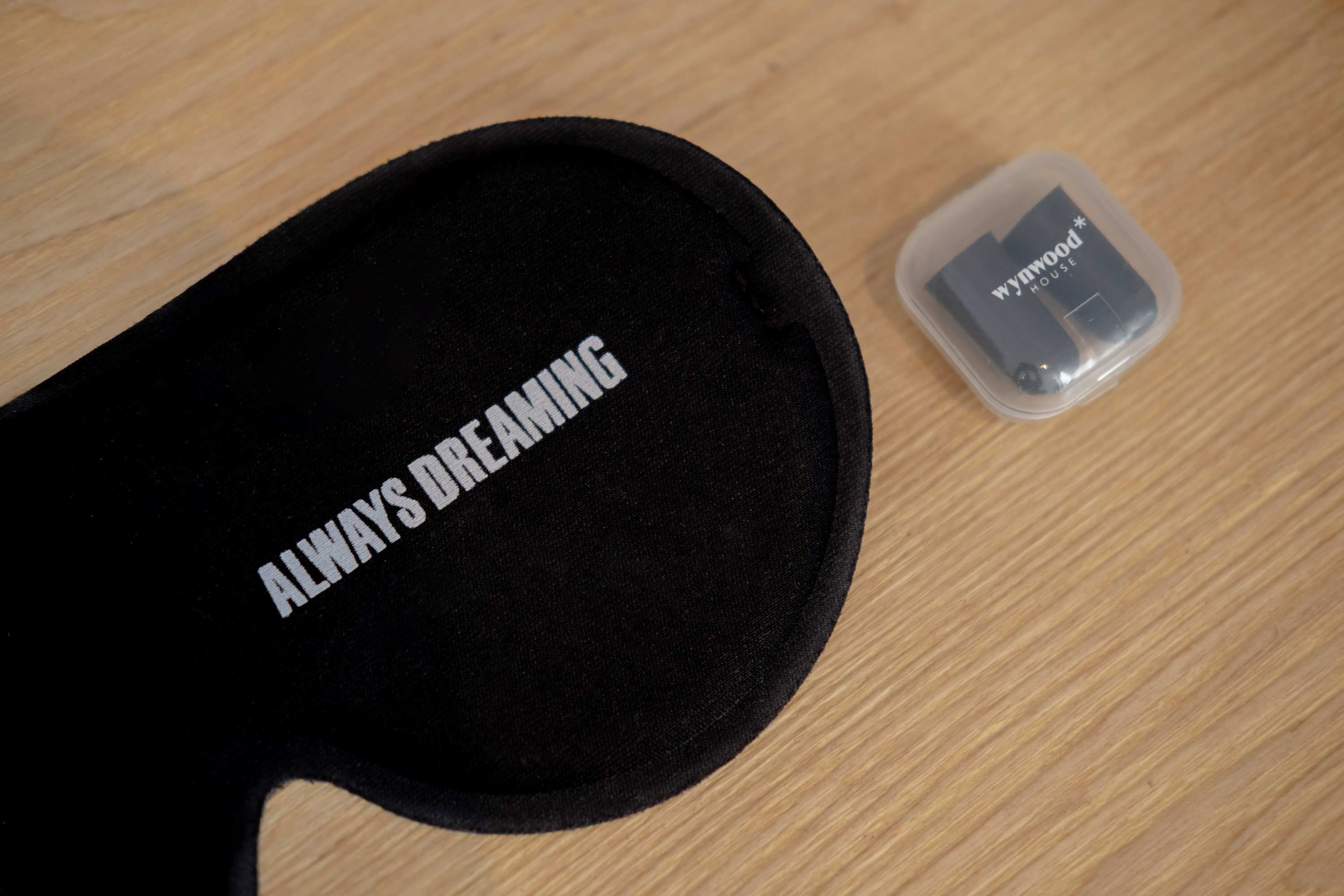 Ein schwarzer Hut mit der Aufschrift "ALWAYS DREAMING" und ein kleiner Kunststoffbehälter mit einem Logo.