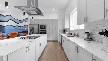 A modern kitchen with white cabinetry, a central island, stainless steel appliances, and a backsplash with a wave pattern.