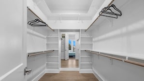 Un pasillo estrecho con paredes blancas y suelo de madera, que conduce a un dormitorio con cama y ventana.
