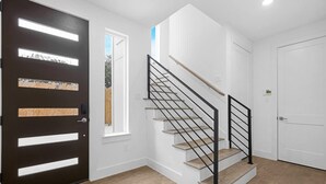 A modern interior with a staircase, a black door with glass panels, and a white wall. - Newly Built Modern 3 Bedroom Houston Home (Houston)