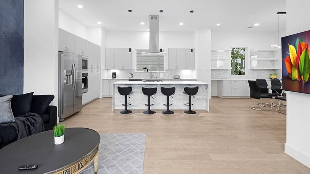 A modern kitchen with a central island, bar stools, and a dining area with a black table and chairs. - Newly Built Modern 3 Bedroom Houston Home (Houston)